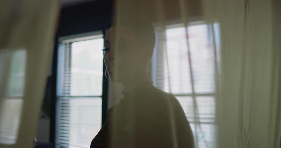 A woman stands in her home and looks out the window