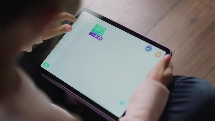 A girl is sitting down holding a tablet computer with one hand and using her other hand to navigate the interface