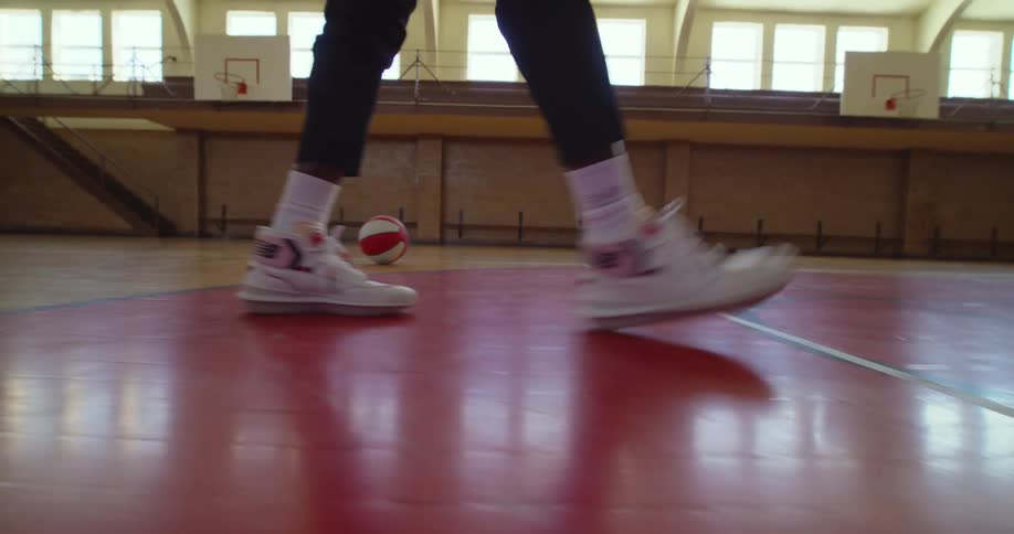 A person wearing white athletic shoes walks across an indoor basketball court