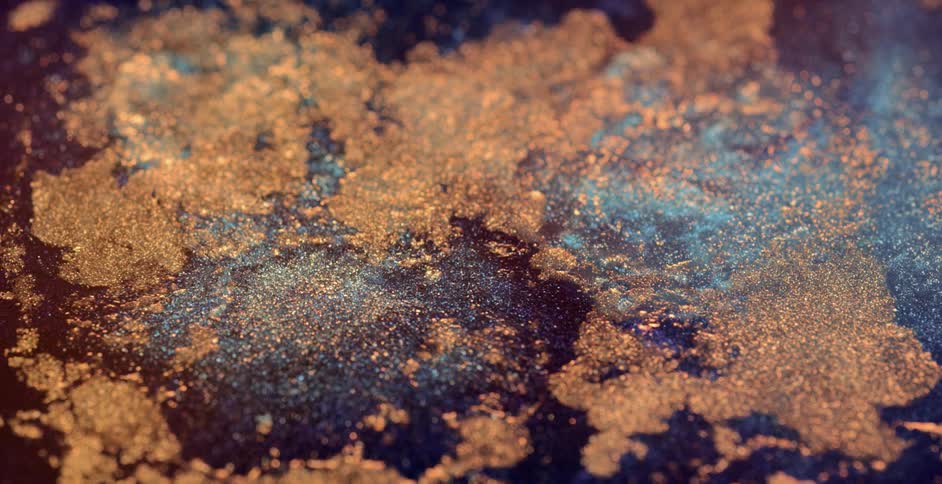 Gold glitter floats on a blue liquid surface and spread as drops fall