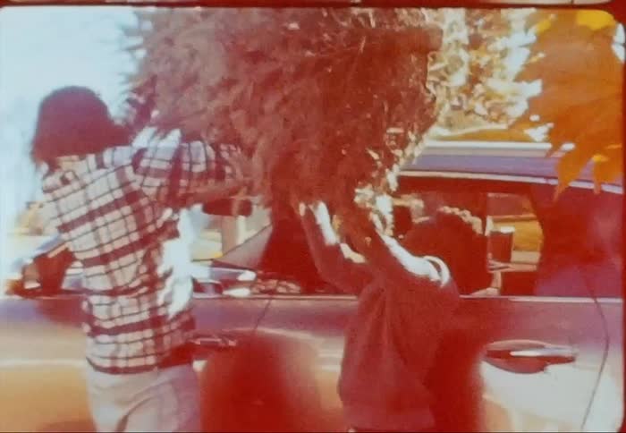 Father and son placing a christmas tree on the roof of a car caught on vintage film