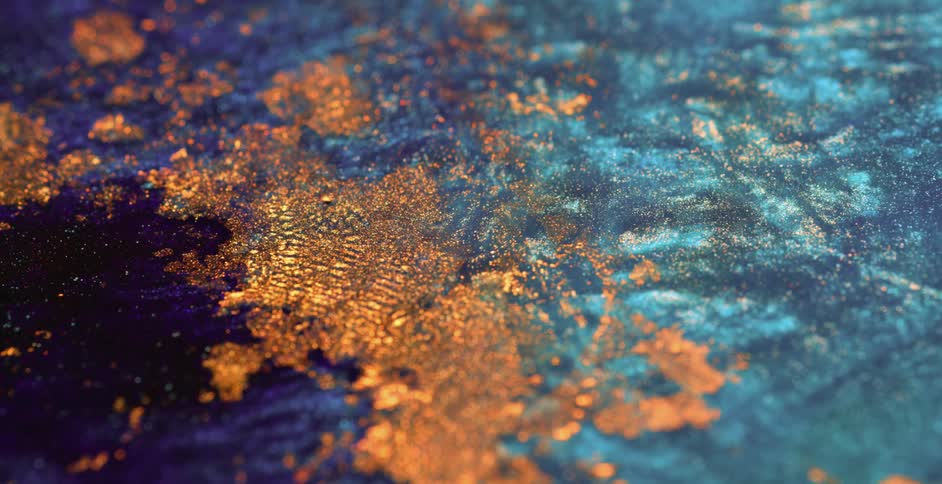Close up of a layer of gold flakes floating and moving over a blue shimmering liquid