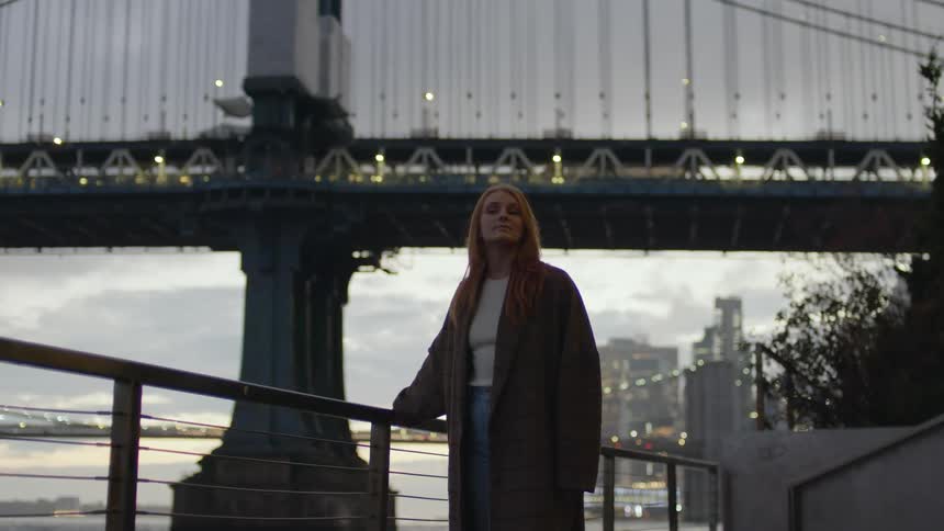 A woman walks across a path on the shore as cars drive across a bridge above her