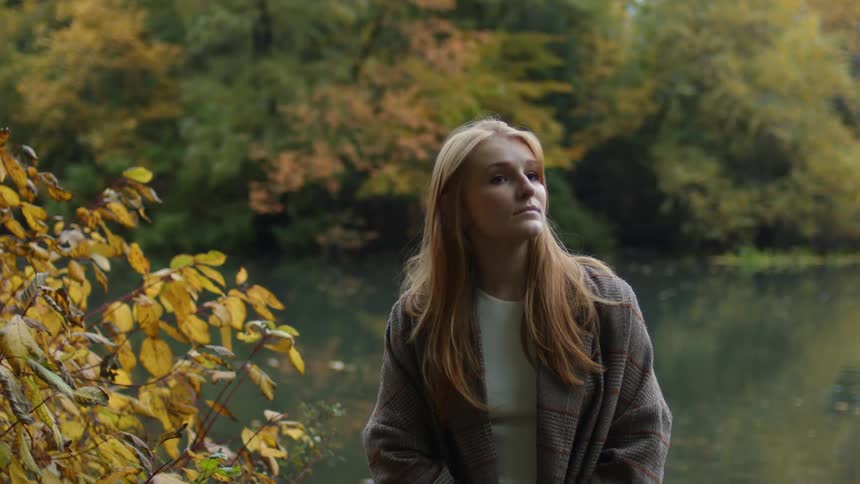 A young woman is posing for the camera in the nature area around fall time