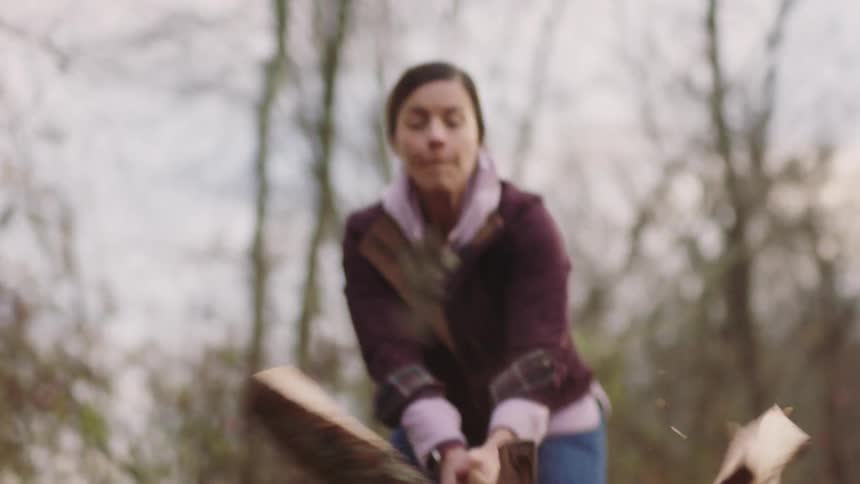 Female splitting wood with an ax in the forest