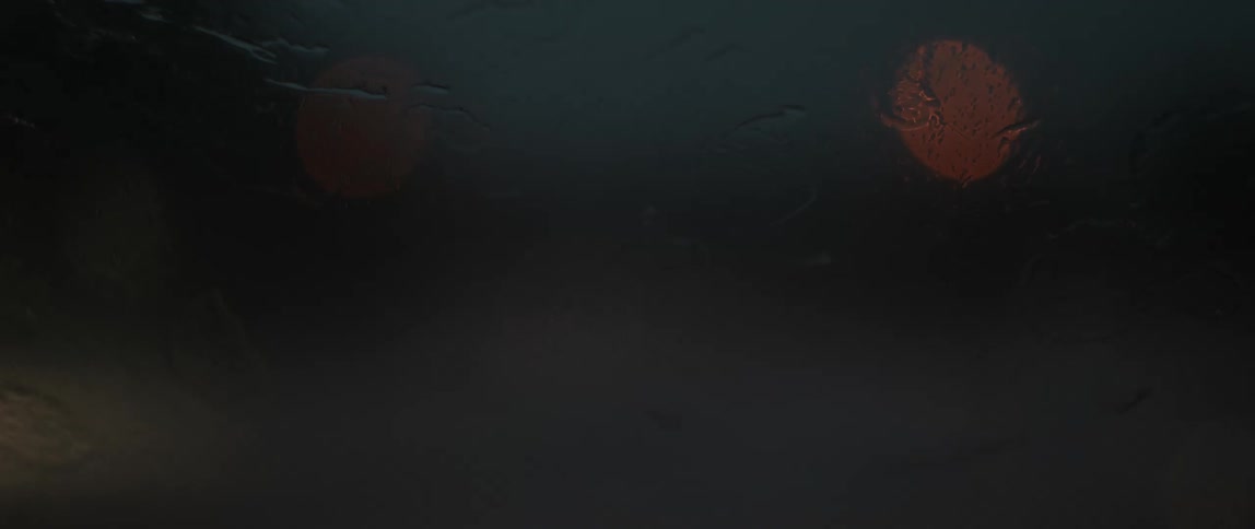 Drops of rain fall on the windshield of a vehicle between swipes of the windshield wipers at night