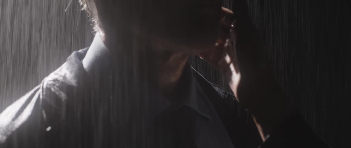 Woman reaches up to cup mans face as they stand in the rain getting wet at night