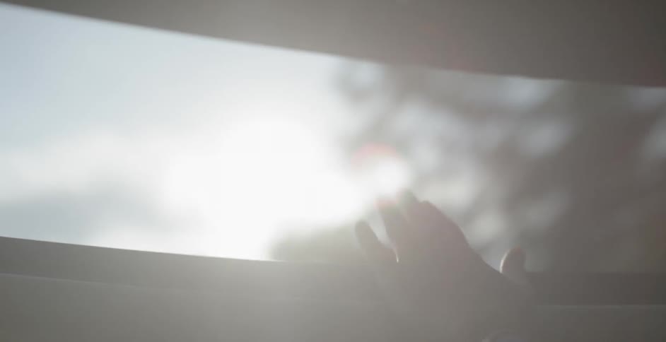 A person sticks their hand out of an open sunroof on a sunny day