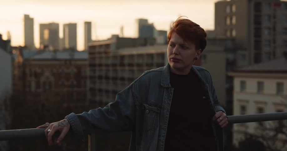 Redhead leans against rail with apartment buildings and skyline in the background