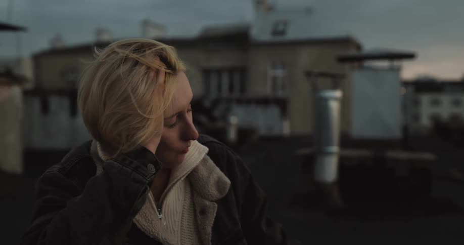 Blonde short haired woman eating and drinking on the roof of a building laughs with a friend