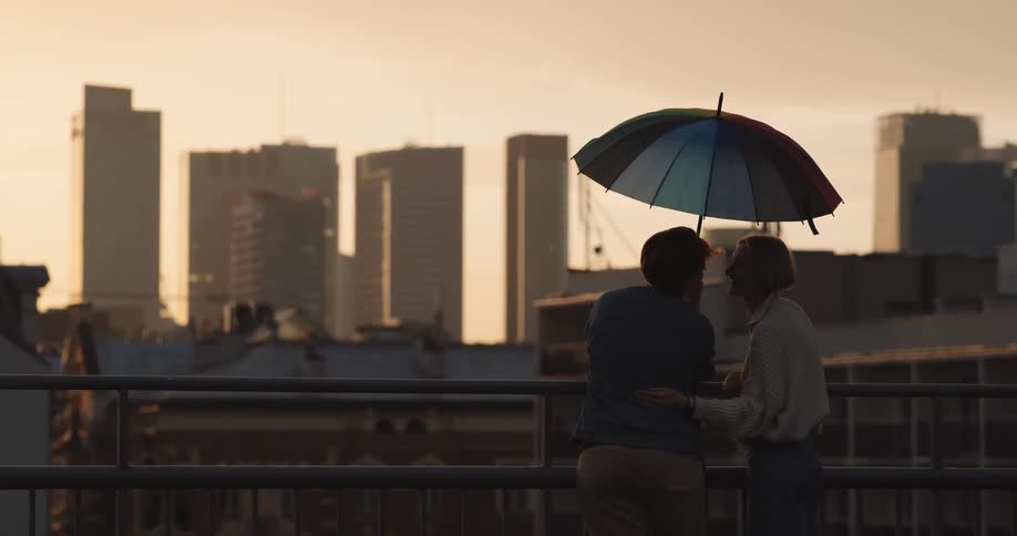 Young couple reclined on a railing under an umbrella looking at the city skyline at evening