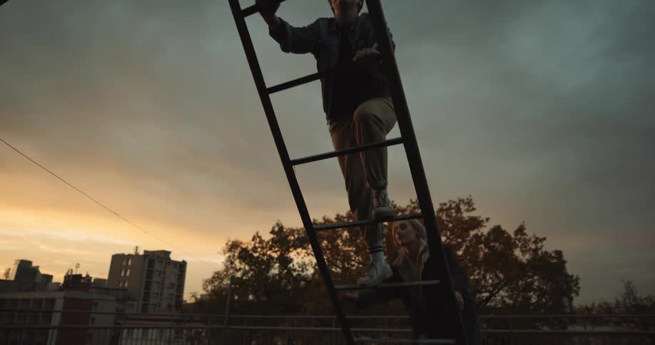A man and woman laugh while climbing up a ladder outside