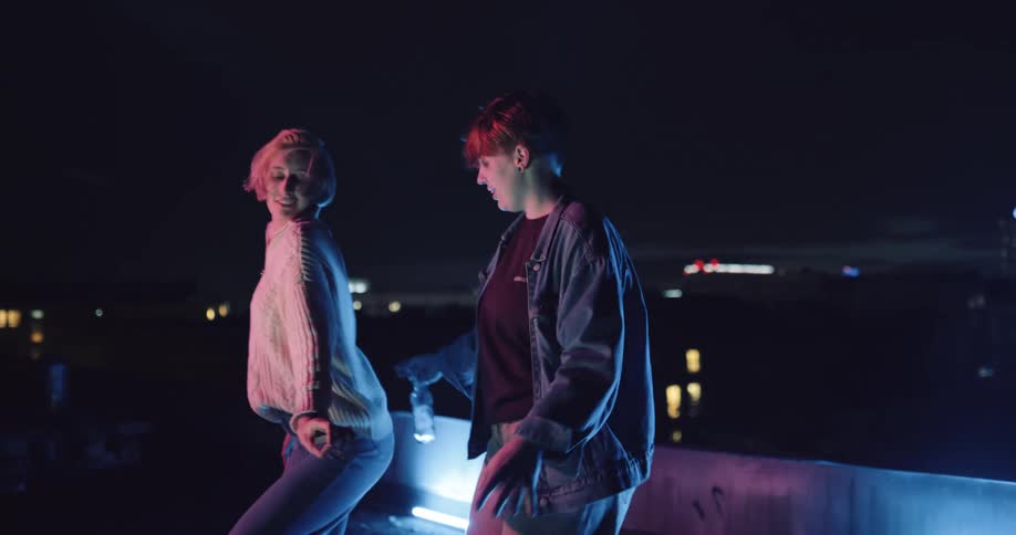 Two women dance at night with city lights in the background