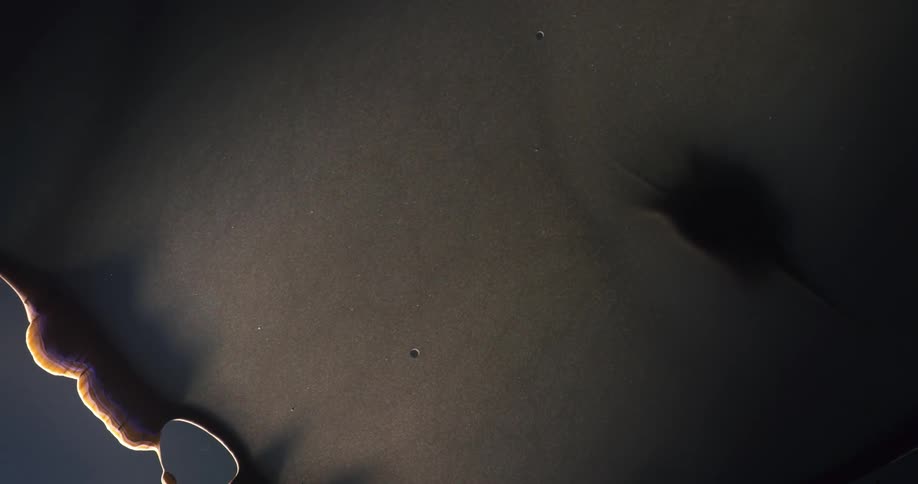 Dark brown mass spreads through fluid and thins until it starts developing holes
