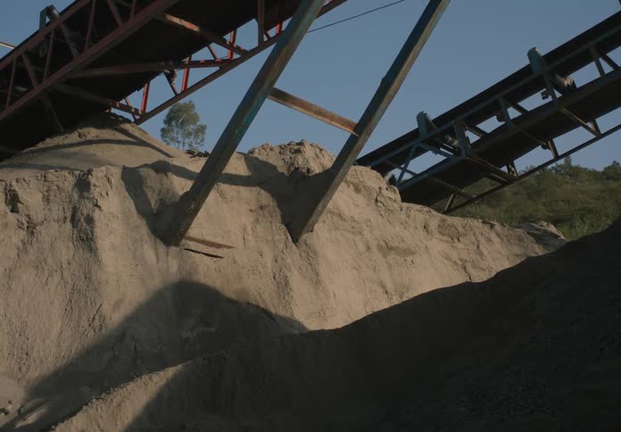 A man walk up a pile of dirt under a conveyor belt