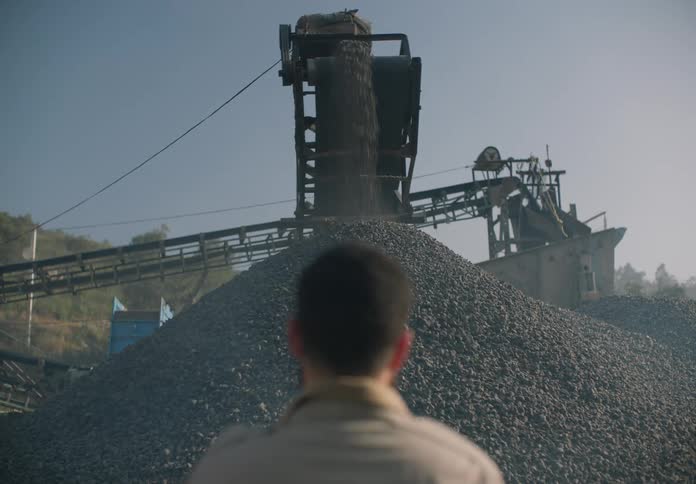 A man watching heavy machinery dumping rocks into a pile outside