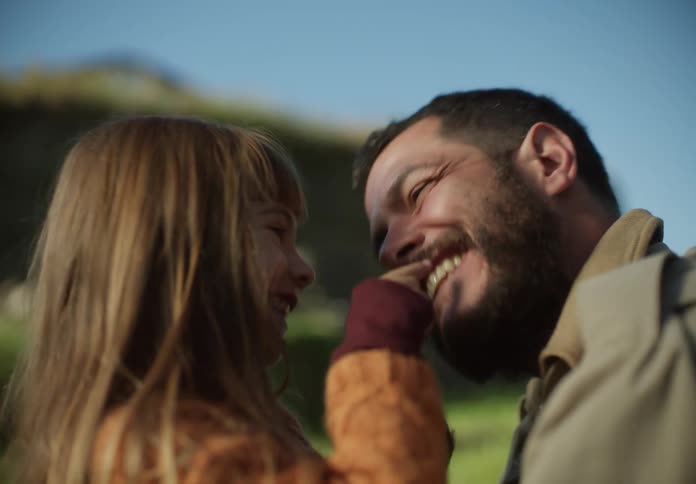 Daughter touches fathers face with beard playing on the grassland