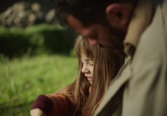 A little girl is sitting outside with her father talking and laughing as she moves her hands