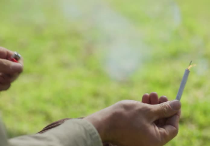 A man is sitting down outside and he pulls a firecracker out of his pocket and lights it with a lighter then he tosses it away