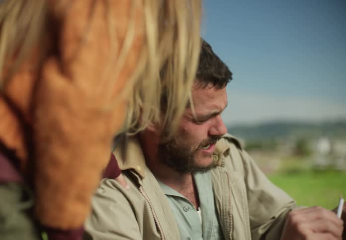 Father with beard and beige jacket plays with daughter on grass in the countryside