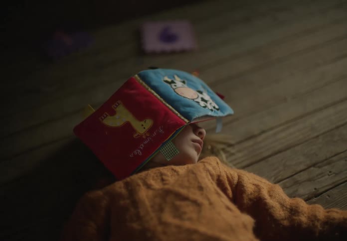 Young child sleeping on hardwood floor with fabric book on their head