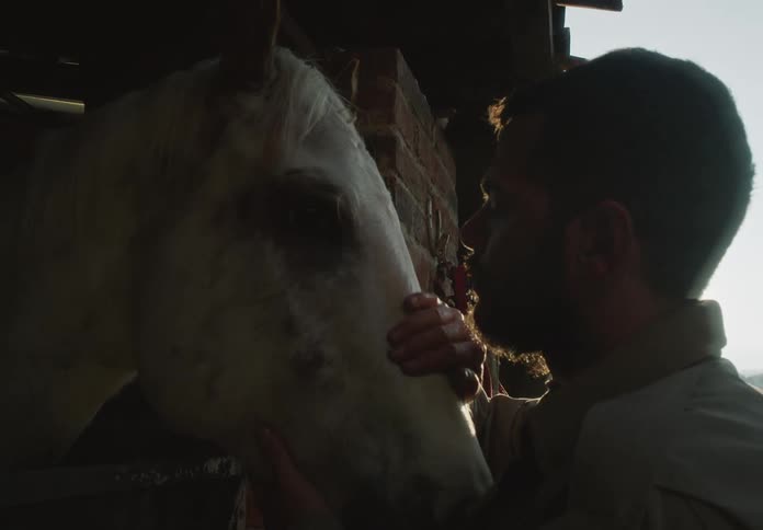 A young white man is petting there horse in the middle of the day