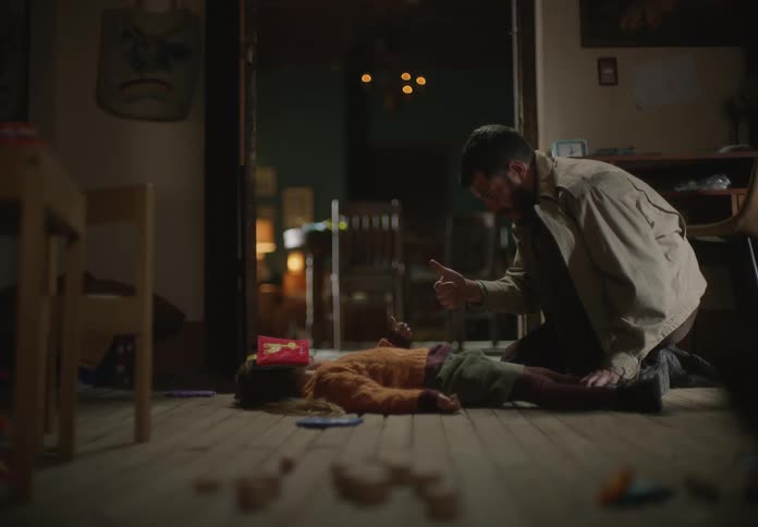 Father and daughter touch thumbs as girl lies on her back on floor with face covered