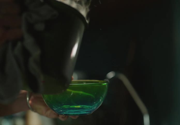 Man uses a towel to pick up a pot of boiling water and pours it in a glass bowl