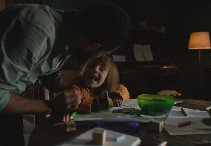 Father and daughter are inside and the kid is coloring a picture