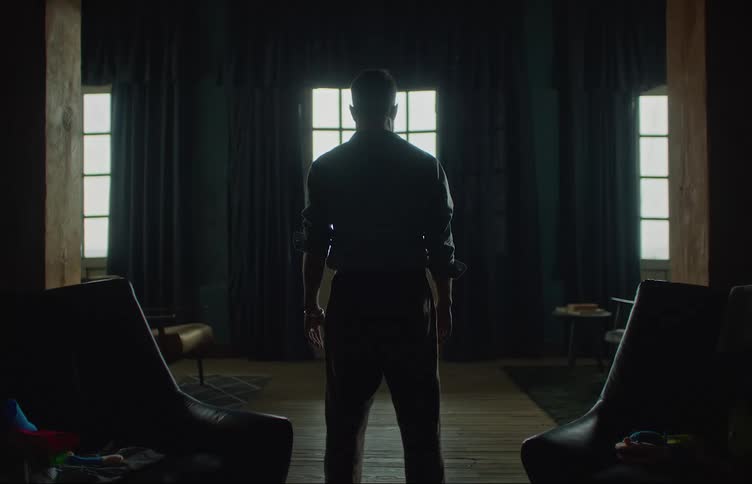 A man is standing in a room between two chairs facing the windows