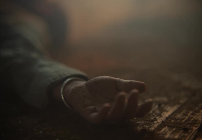 Close up of a womans hand covered in dirt as she lies on the ground motionless