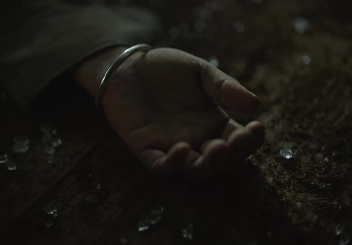 A persons hand is on the ground surrounded by broken glass