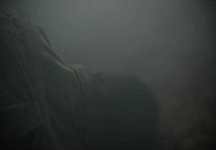 A person lies on their side in a smoke filled room