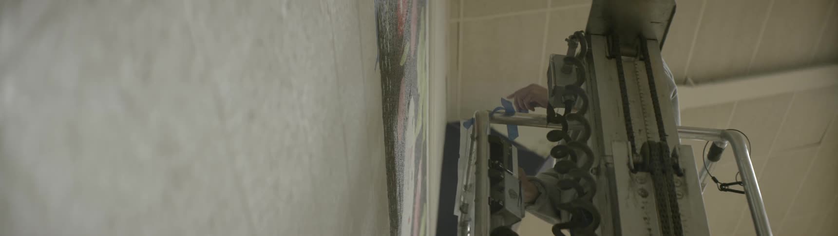 A person rises on a lift and puts tape on a wall