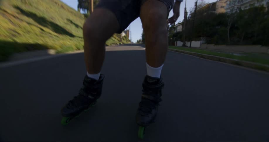 A man skates down a road through a neighborhood using inline roller skates