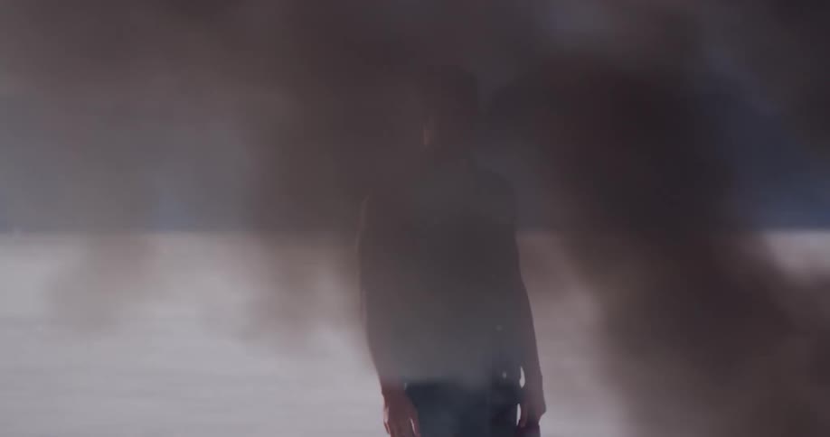 A man stands still behind a billowing cloud of smoke from something on fire