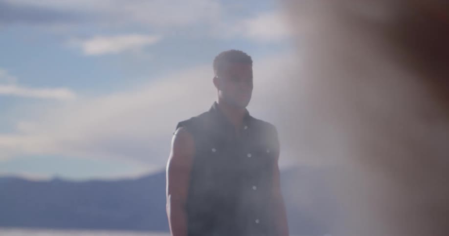 Man stands on desert plain staring as fire produces thick clouds of black smoke