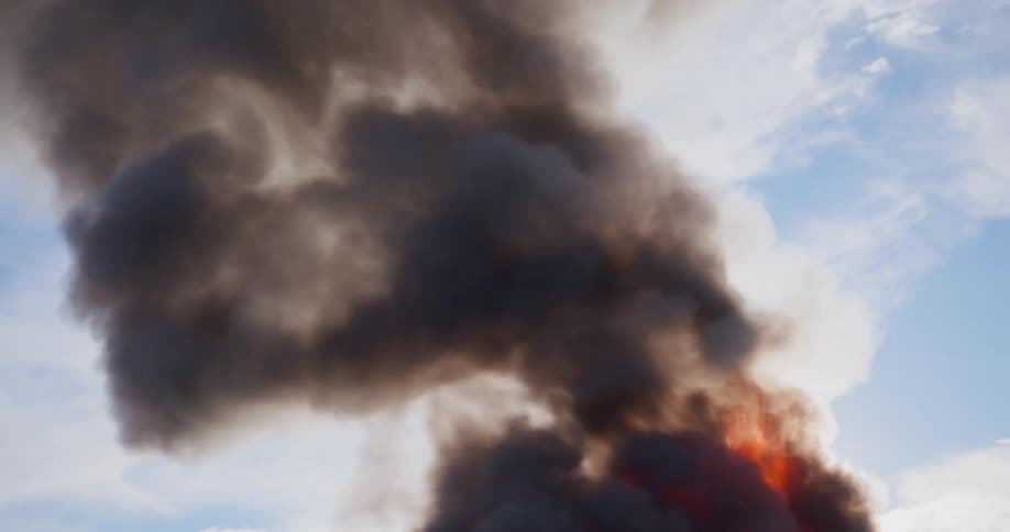 A blazing fire sends dark smoke billowing into the sky during the day