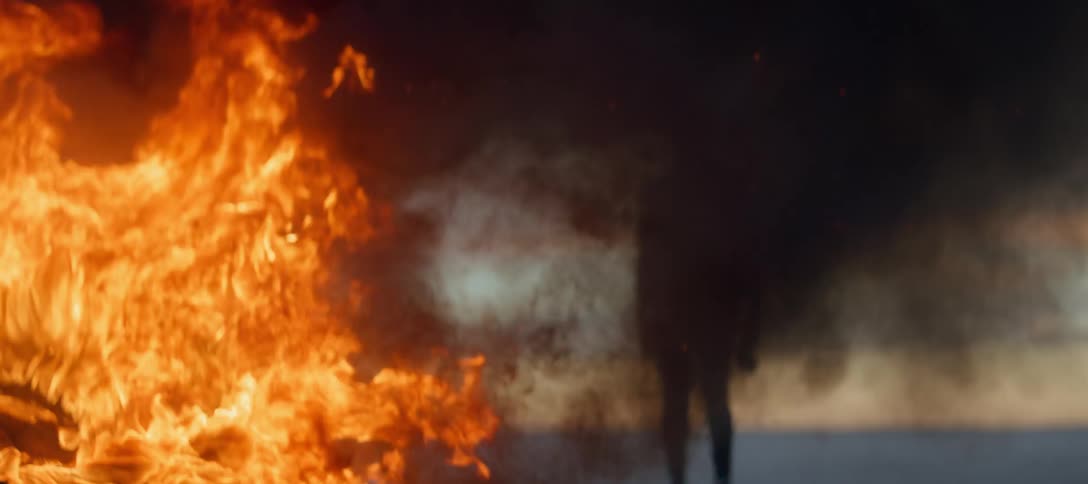 A young man is standing outside by a fire in the middle of the day