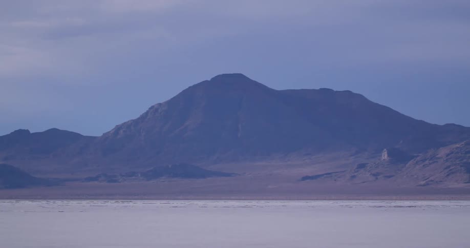 A mountain range looms over an arid and barren flatland during the day