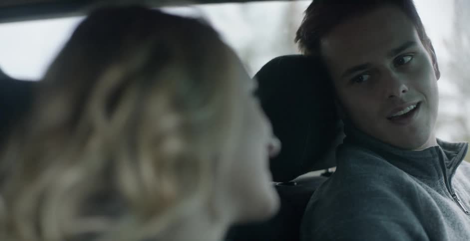 A man and woman chat and smile at each other while they sit in a car