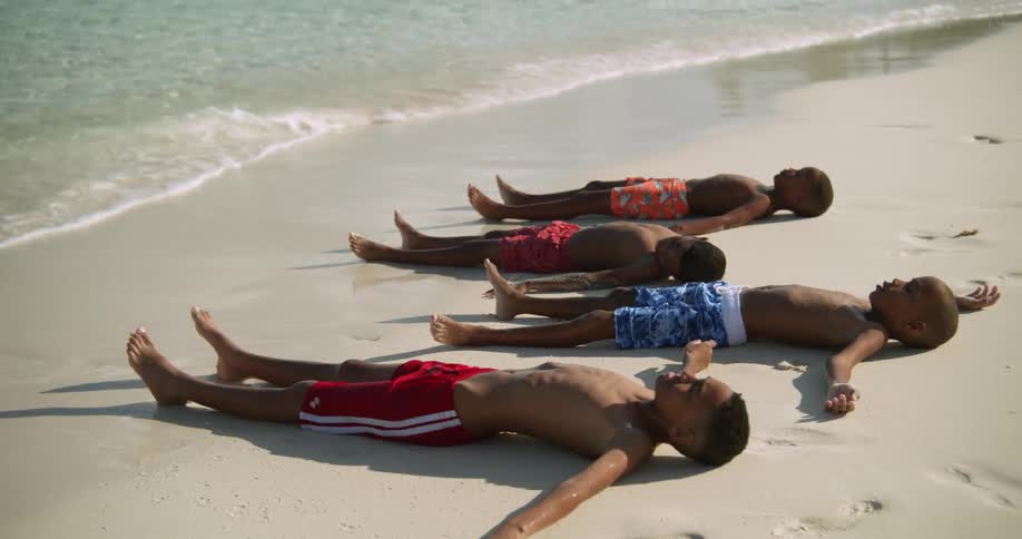 A few kids are at the beach and are laying down on the sand