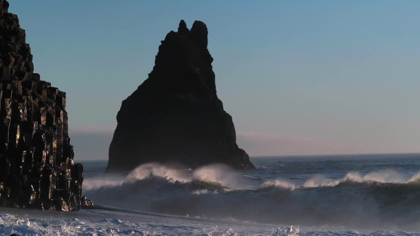 Waves crash around tall rocks at Black Sand Beach Reynisfjara