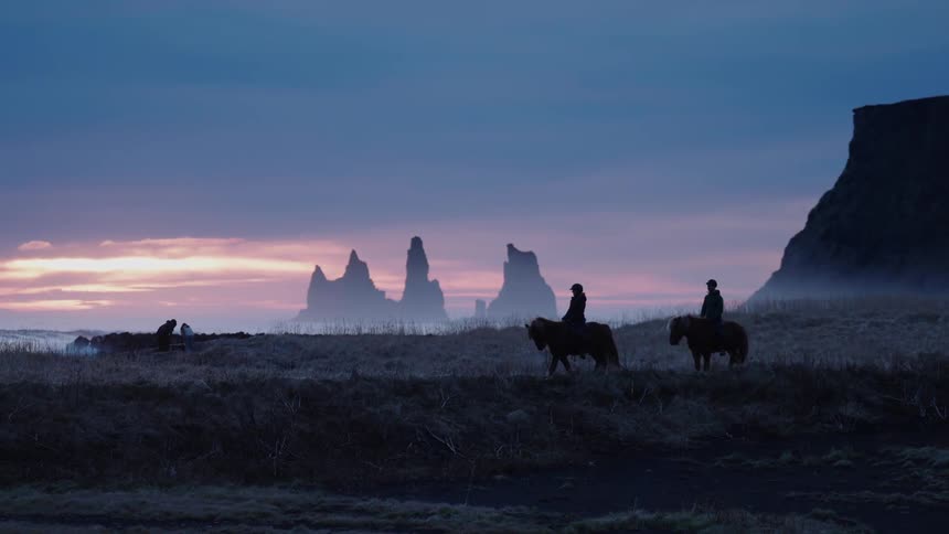 Iceland Two people are riding horses while the sun is setting