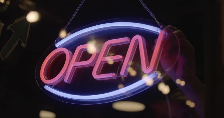 A man turns on a neon open sign in a store window