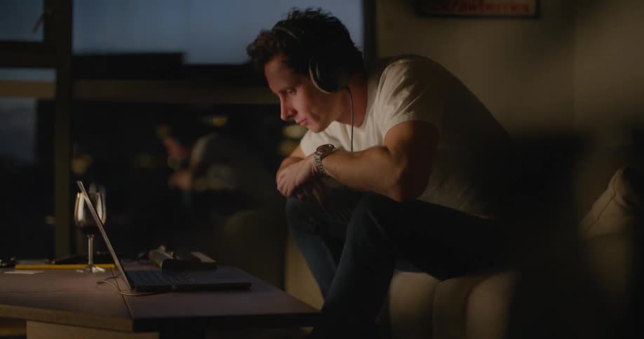 Man sits on couch in apartment using short keyboard and laptop at night