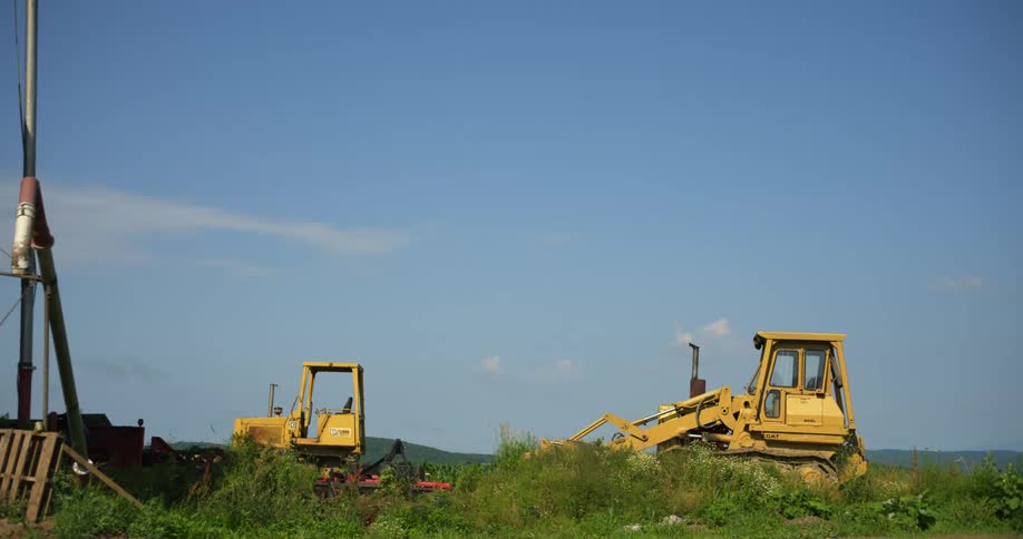Two pieces of heavy construction equipment sit parked in field