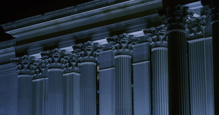Light illuminates details of columns on building with classical architecture at night
