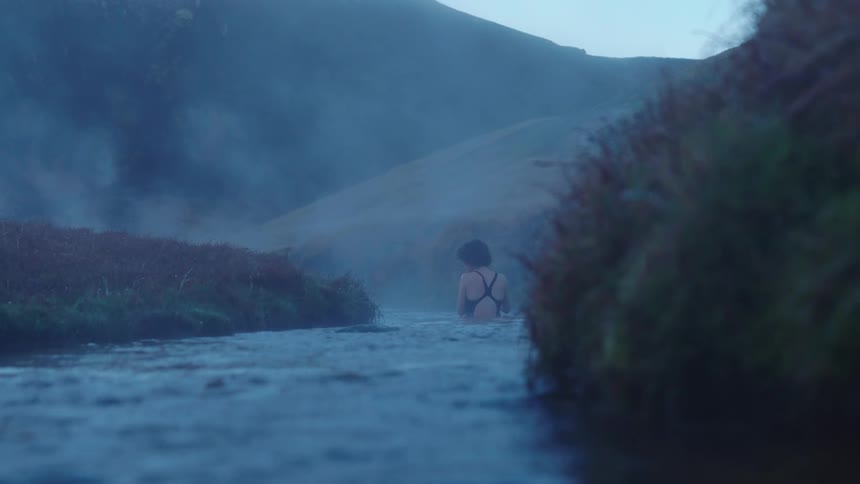 Woman wearing a swimsuit standing on a river surrounded by mist at morning