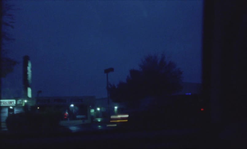 Street stores on a small town at night seen from a moving vehicle caught on vintage film